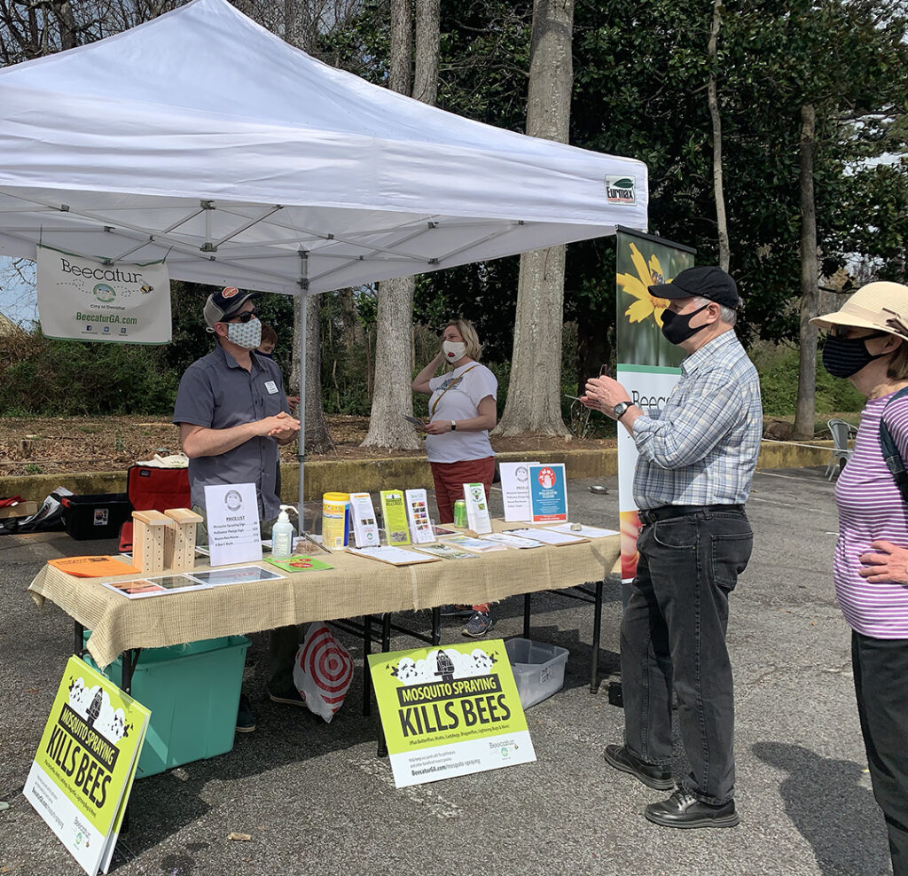 Bee City volunteers at a booth with signs and printed materials about mosquito management without spraying