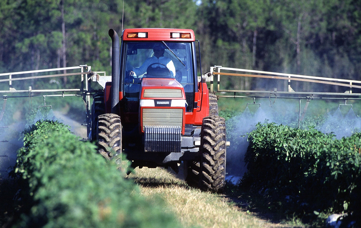 Tractor applying pesticides to rows of crops