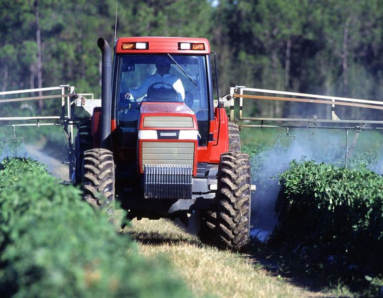 Tractor applying pesticides to rows of crops
