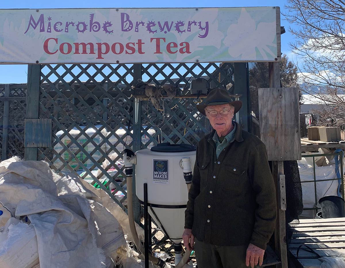 Mikl Brawner standing in front of the compost tea brewer at Harlequin's Gardens