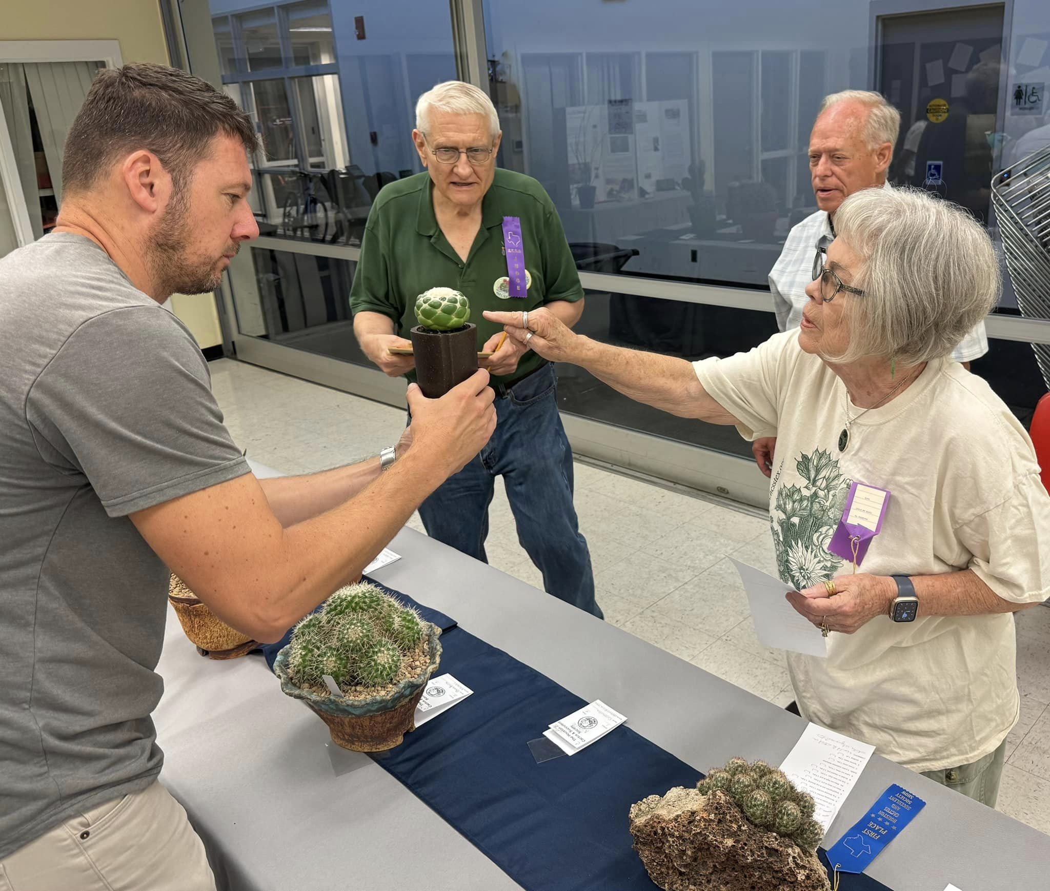 A man holds a potted cactus for 3 judges to view at a plant show and sale