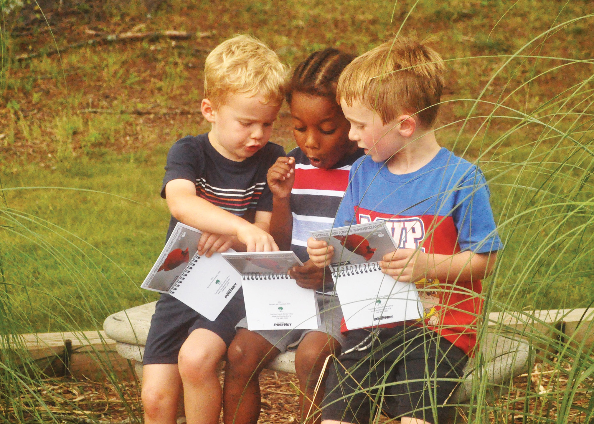 Three young boys excitedly look at their activity booklets. Two of the boys are white, one is Black