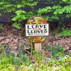 A sign reads "Leave the Leaves" surrounded by violets, leaf litter, and shrubbery