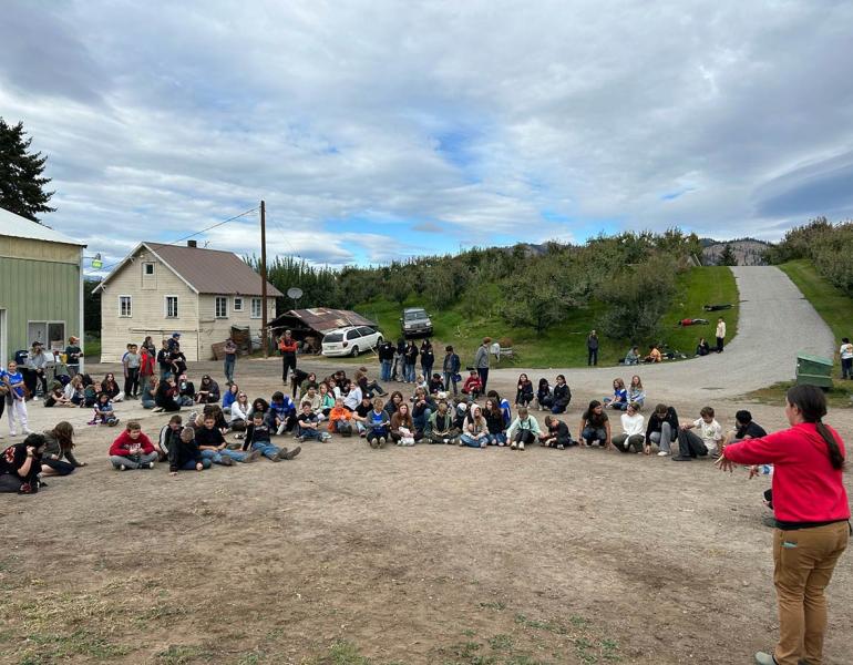 Over a hundred students circle around a speaker, listening to instructions for the day