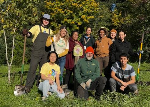 10 people in work clothes with shovels gather around a pollinator habitat sign in a garden.